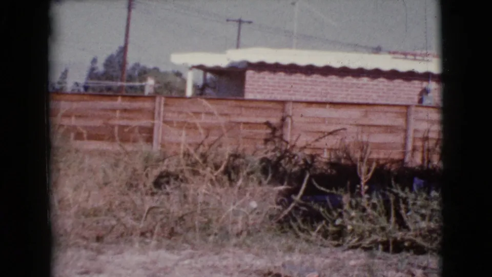 Final 1964 Cottonwood, Arizona frame showing dry vegetation, a wooden fence, roof edge, and background utility poles.