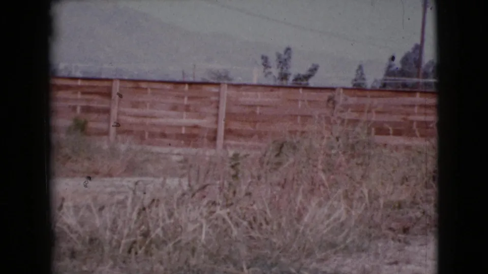 1964 Cottonwood, Arizona frame showing a weathered fence across dry grass, with utility lines and faint mountains beyond.
