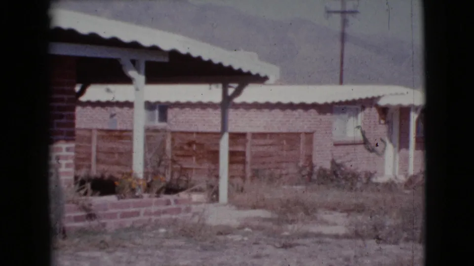 1964 Cottonwood, Arizona frame showing a modest brick house exterior with a covered porch and corrugated roof.