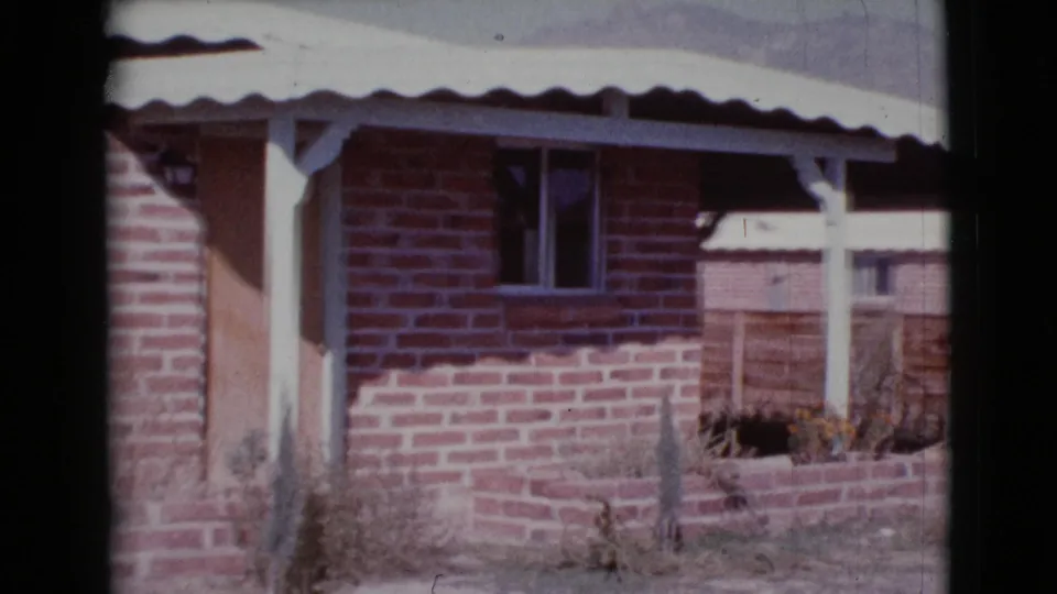1964 Cottonwood, Arizona frame with a brick house corner, shaded wooden door, small window, porch support, planter, and backyard fence.