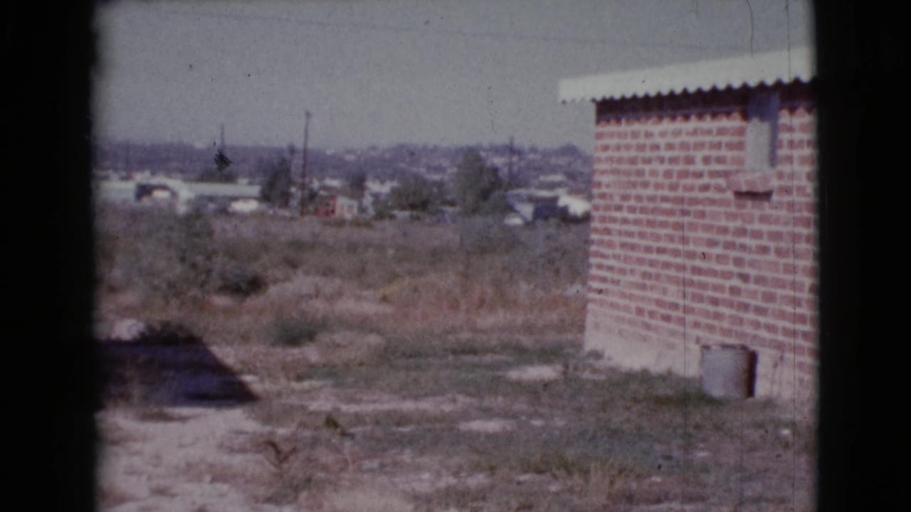 Dry field and brick building with scattered houses visible in the distance.
