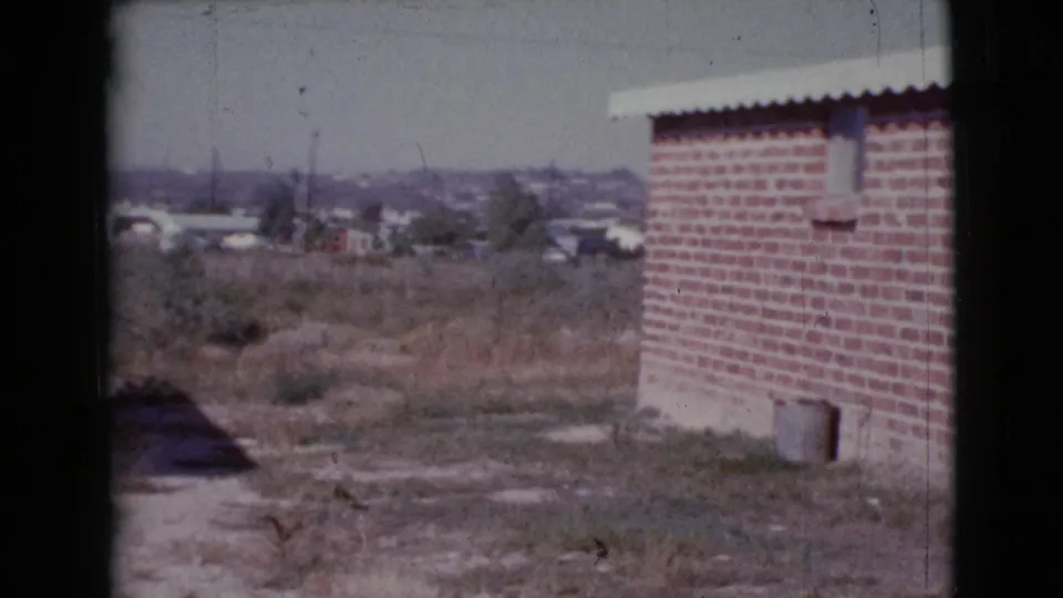 1964 Cottonwood, Arizona frame with a brick wall on the right, scrubby vacant ground, and homes across the background.
