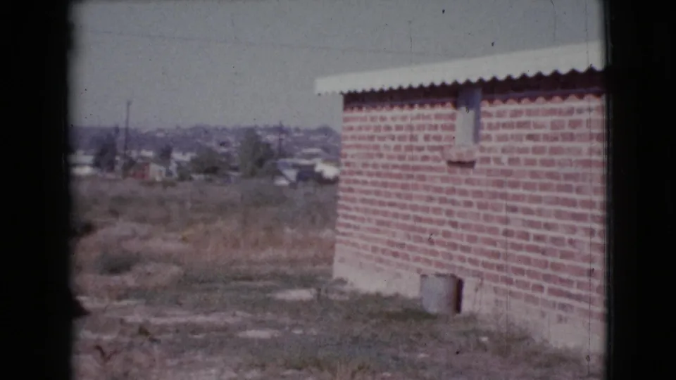 Final 1964 Cottonwood, Arizona frame showing the brick building edge, dry field, and low houses in faded 8mm color.