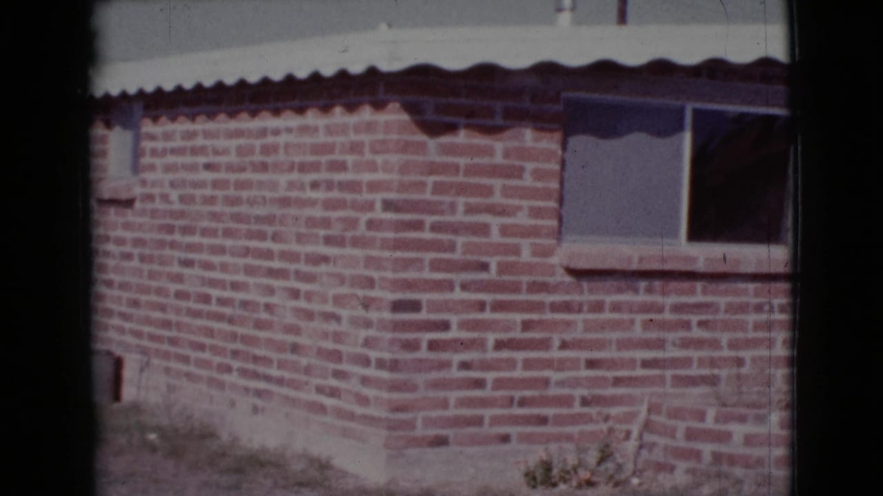 Red brick house wall with a small window and roof edge in sunlight.