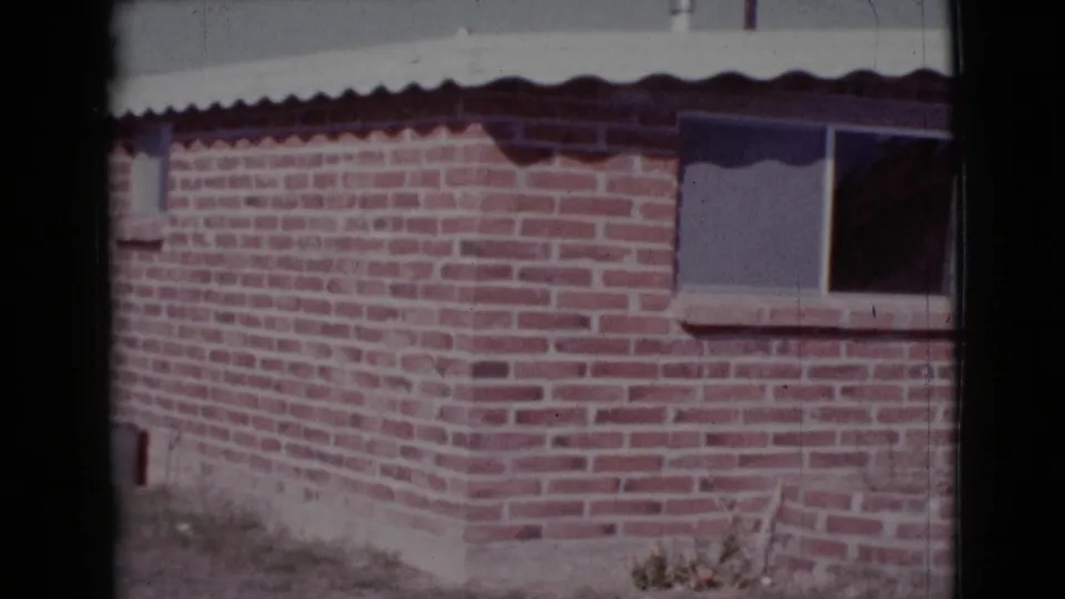 1964 Cottonwood, Arizona 8mm frame showing a red brick house exterior, small window, dark curtain, and roof edge.