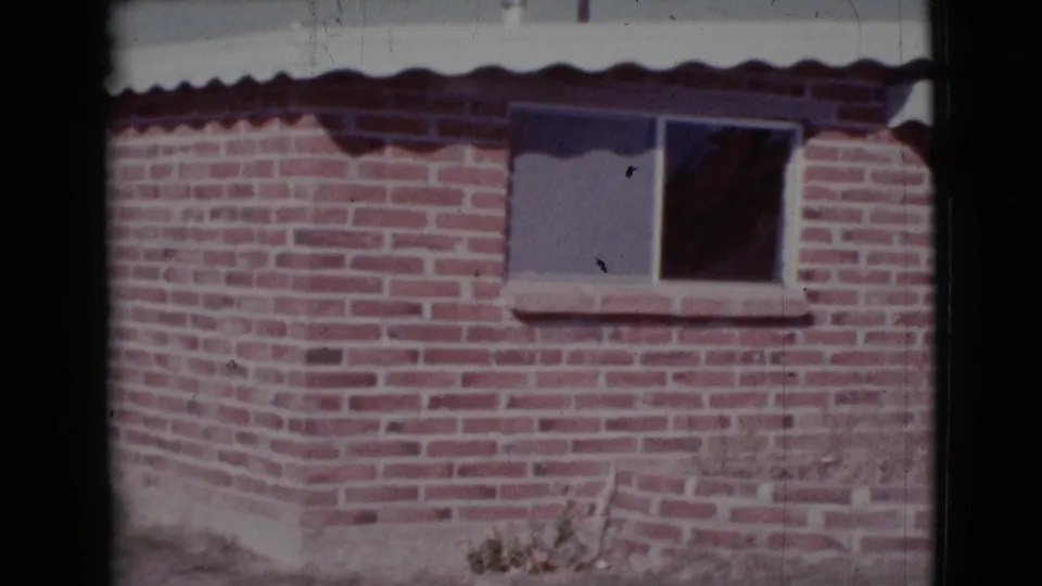 1964 Cottonwood, Arizona frame of a brick house corner, window with dark curtain, and sunlit exterior wall.