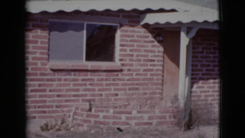 1964 Cottonwood, Arizona frame showing the house facade with brickwork, a small window, roof edge, and right-side doorway area.