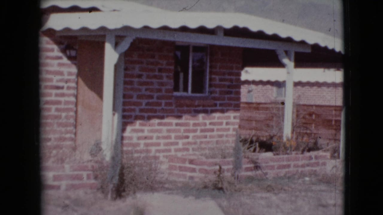 Brick house exterior with white corrugated awning, porch posts, small window, and dry yard.