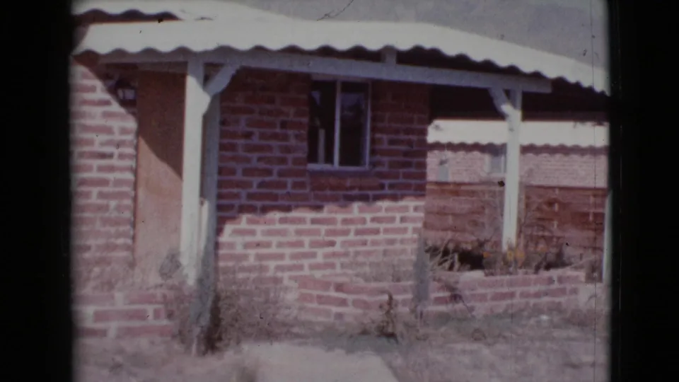 1964 Cottonwood, Arizona home exterior with red brick facade, white awning, porch supports, low planter, and sparse dry yard.