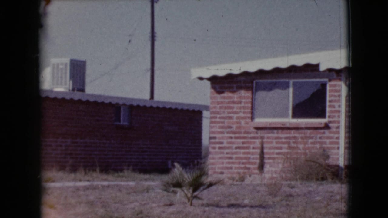 Brick house exterior with white awning, window air conditioner, low wall, and dry yard plant.