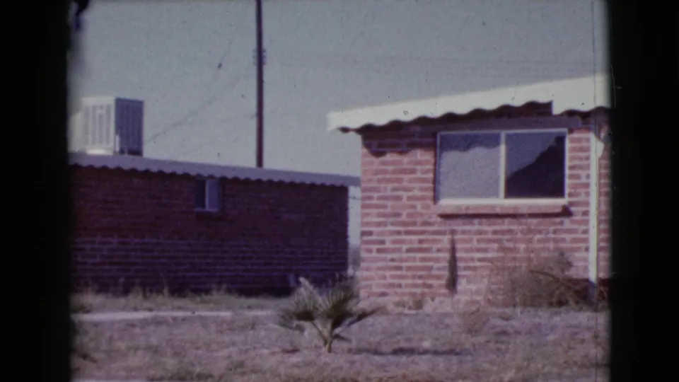 1964 Cottonwood, Arizona home-movie frame of a modest brick residence with a white awning and sparse dry yard.