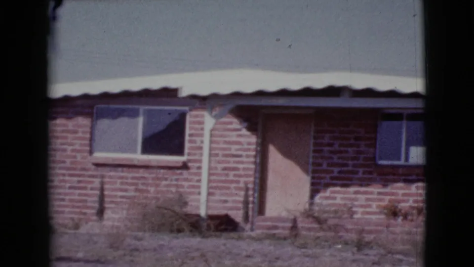 1964 Cottonwood, Arizona 8mm frame showing the brick house at the end of the pan, with boarded entry, windows, metal roof, and dry yard.