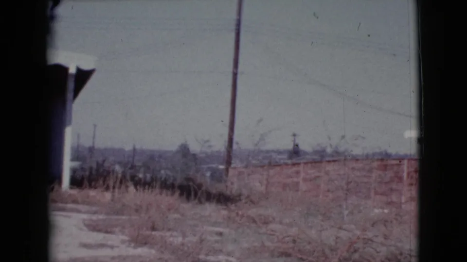 1964 Cottonwood, Arizona frame showing the end of the pan with dry vegetation, low wall, utility pole, overhead line, and a sliver of house.