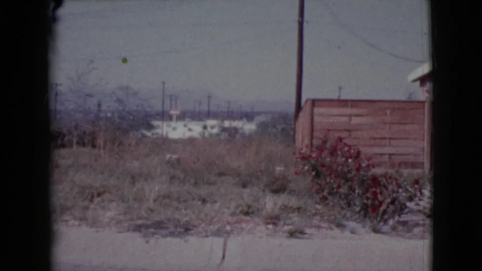 Cottonwood, Arizona field view from 1964 with dry grass, red shrubs, a wooden fence, utility poles, and distant low buildings.