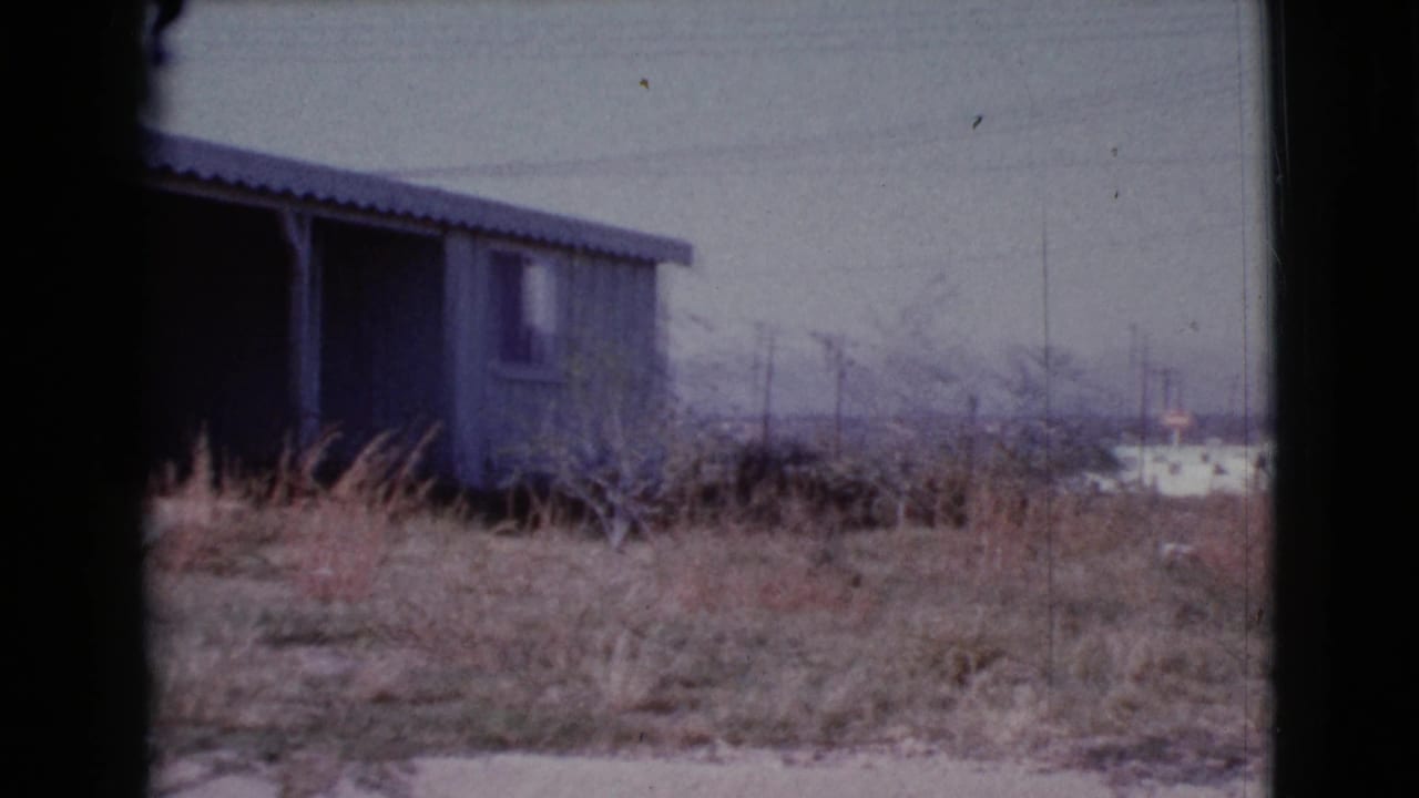 1964 Cottonwood, Arizona frame showing the side of a modest porch-front house with dry grass and distant utility poles.