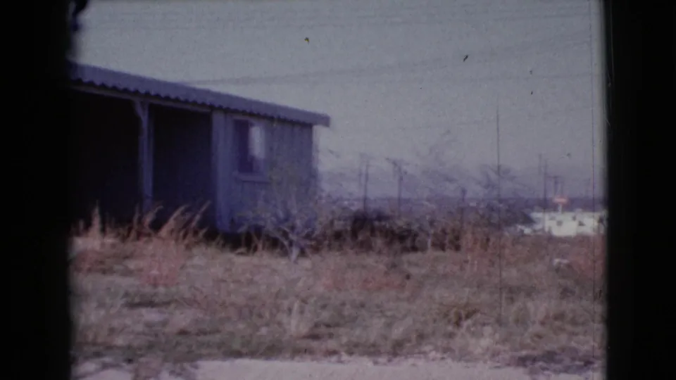 1964 Cottonwood, Arizona frame showing the side of a modest porch-front house with dry grass and distant utility poles.