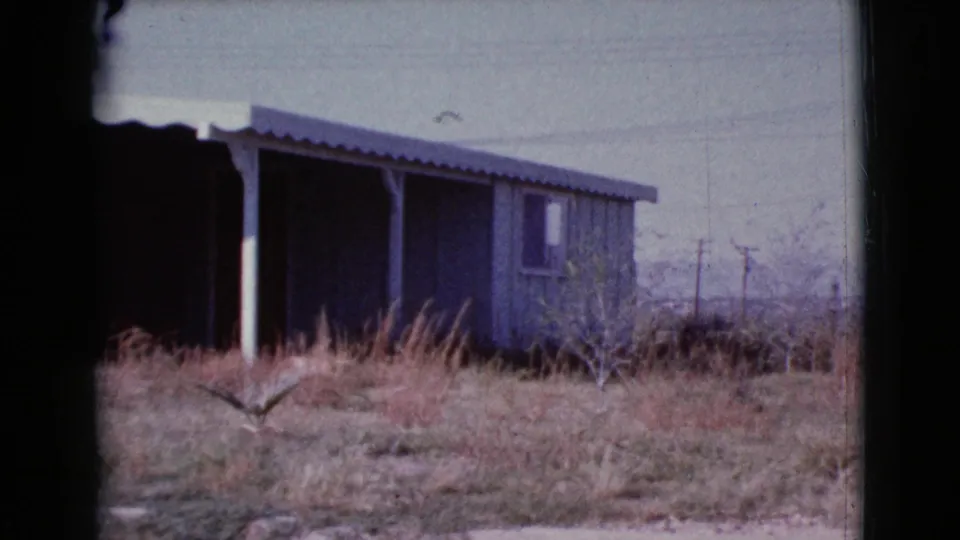 1964 Cottonwood, Arizona view of a weathered porch-front house, dry overgrown yard, and sparse background structures.