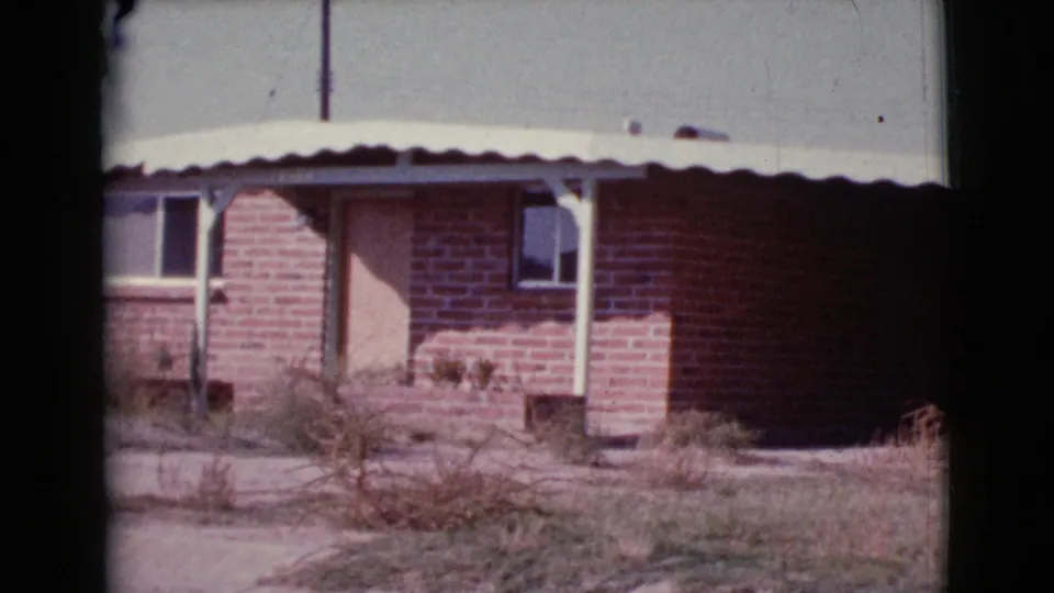1964 Cottonwood, Arizona frame showing a brick house front with a plain door, windows, porch supports, and dry yard.