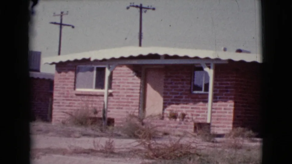 1964 Cottonwood, Arizona 8mm frame of a brick ranch-style house with utility poles visible above the roofline.