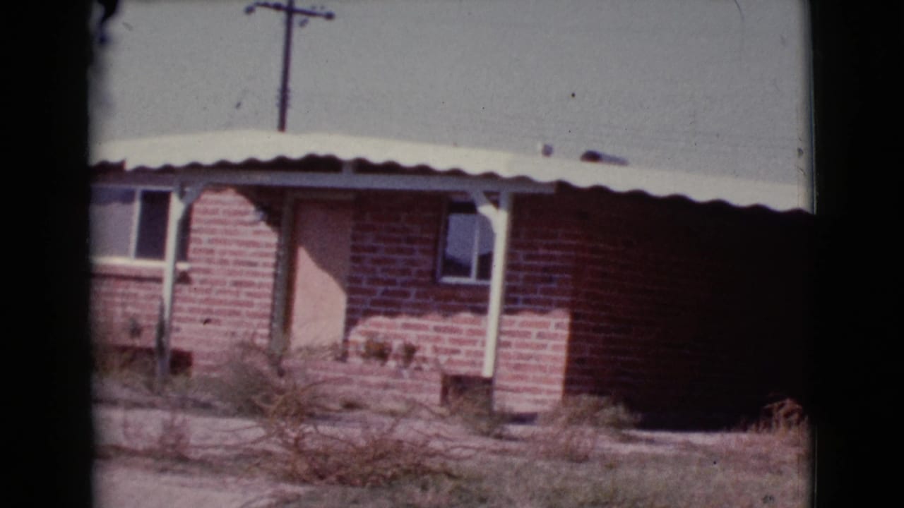 Red brick house exterior with awning, door, window, dry grass, and utility pole.
