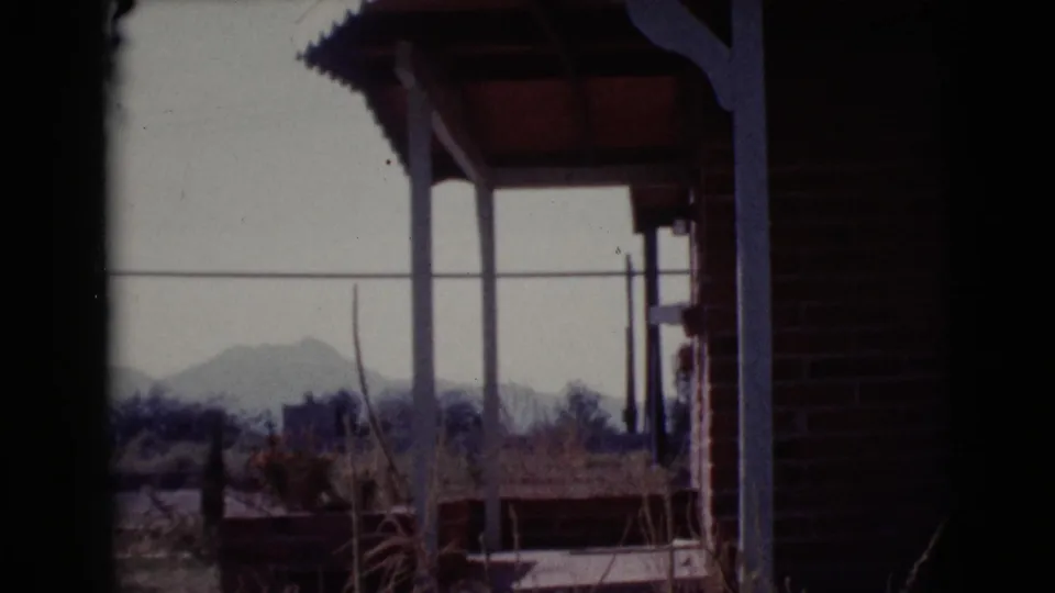 1964 Cottonwood, Arizona porch view with brick wall, roof posts, dry plants, fence lines, and distant low hills.