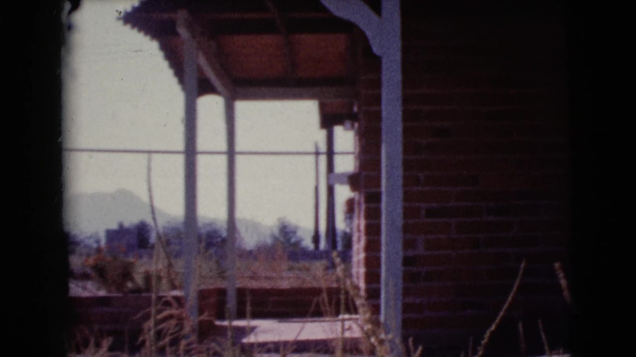 Red brick porch corner with white posts, dry grasses, bright sky, and distant hills.