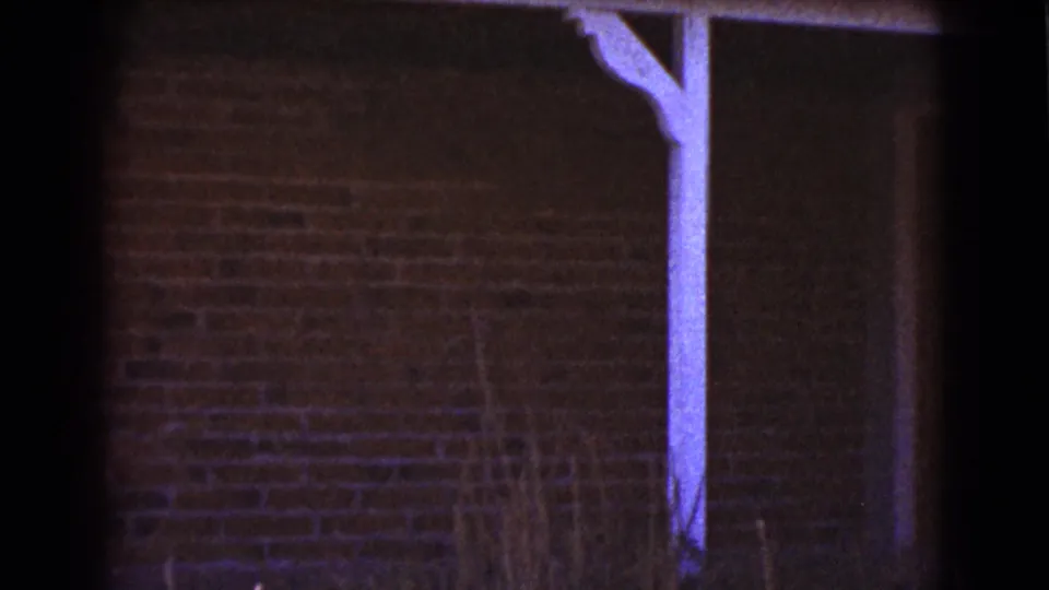 The camera holds on a Cottonwood house exterior, with brickwork, a white porch beam, and a dark doorway or wall edge.