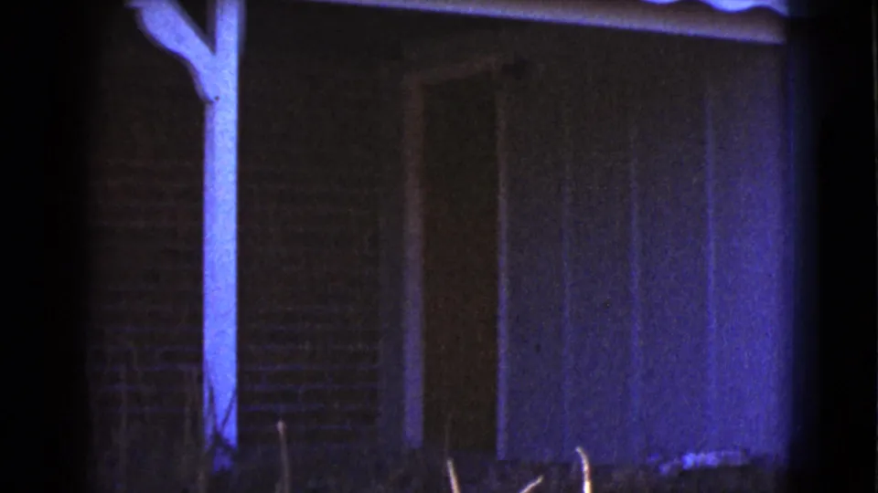 Final 1964 Cottonwood frame shows the porch beam, brick exterior, doorway, and a blue-purple cast across the side wall.