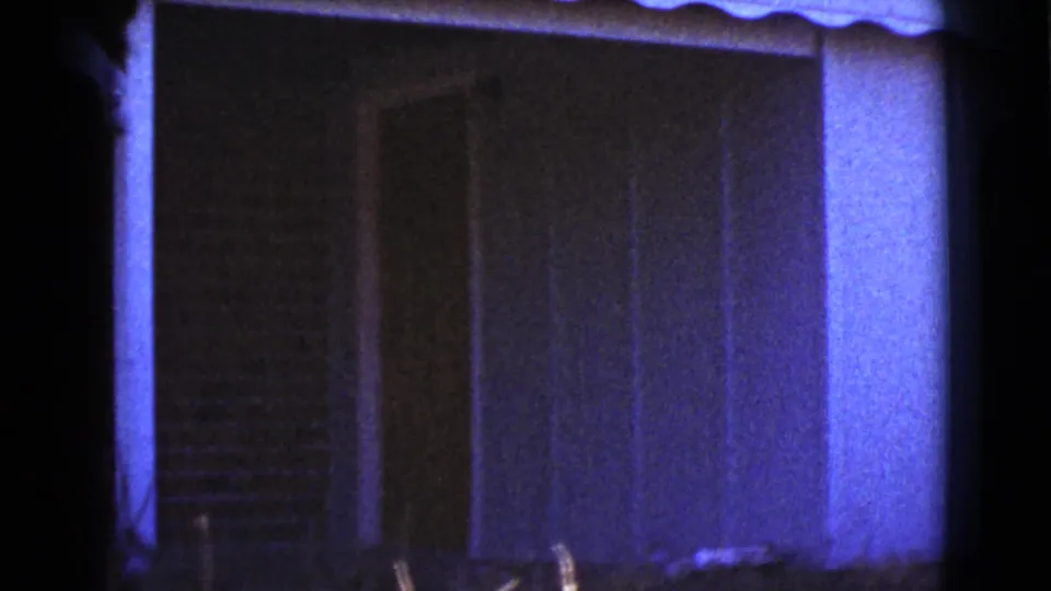 1964 Cottonwood, Arizona home-movie frame showing a small house exterior with vertical siding and dark shaded window area.