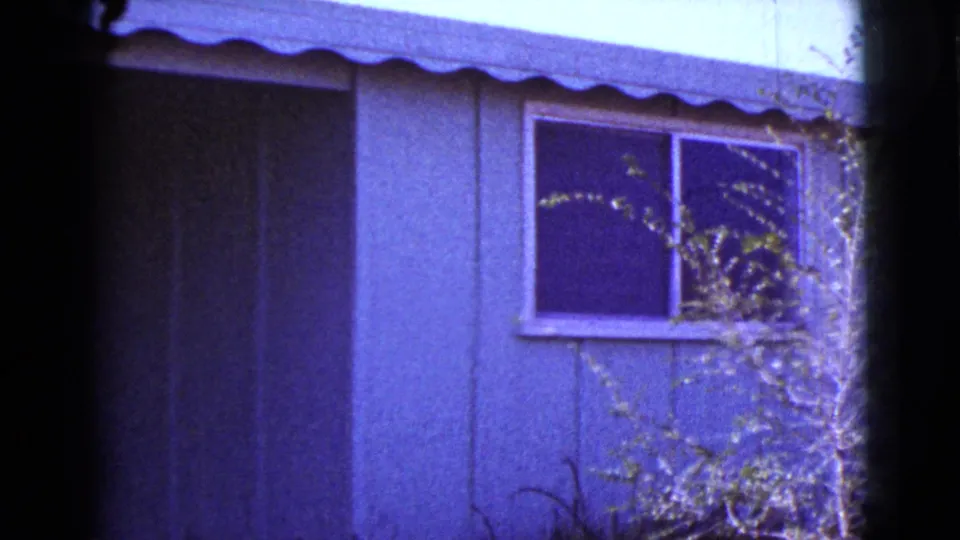 1964 Cottonwood, Arizona home-movie still showing a small house window beneath a scalloped awning with brush in front.