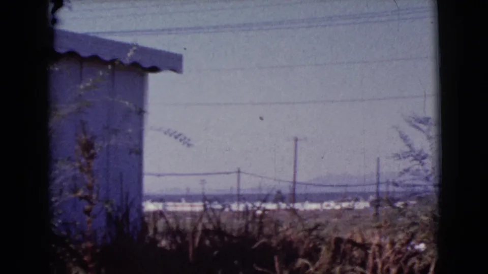 Final frame shows the blue house at the left edge and a flat Cottonwood landscape with brush, utility poles, power lines, and distant structures.