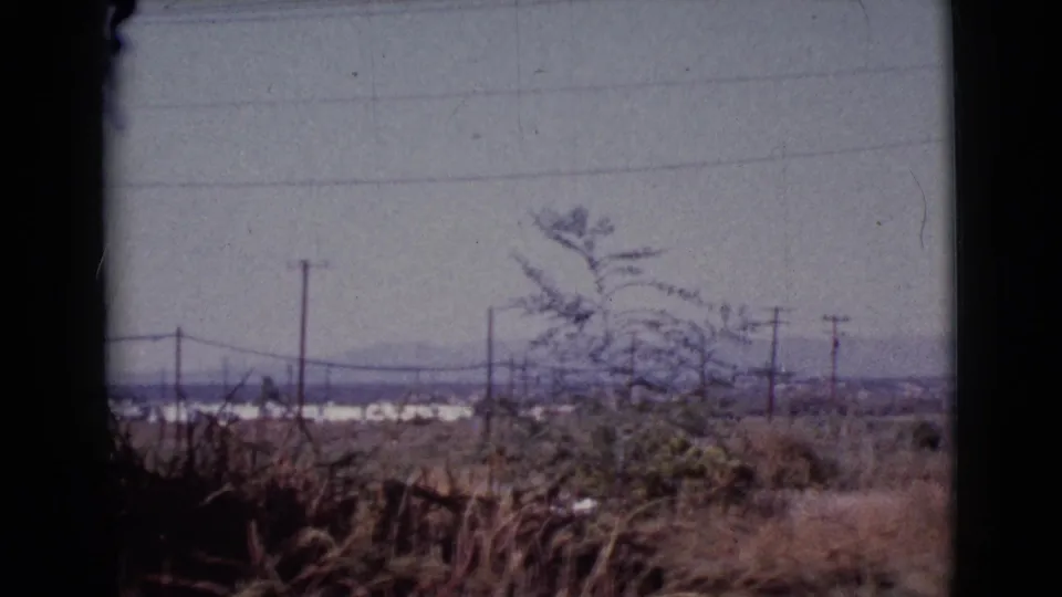 Cottonwood, Arizona rural horizon on 8mm film, with foreground brush, power lines, distant white structures, and low mountains.