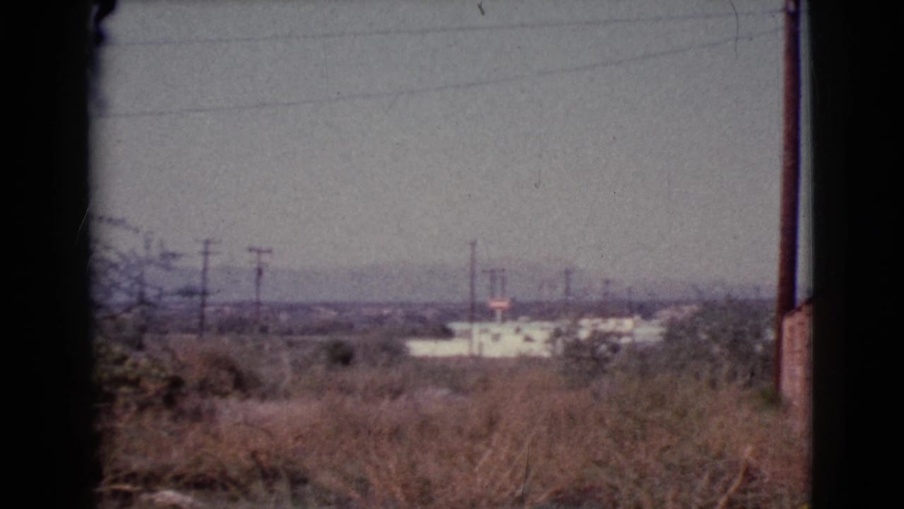 Dry grass and utility poles with distant low buildings under a hazy sky.