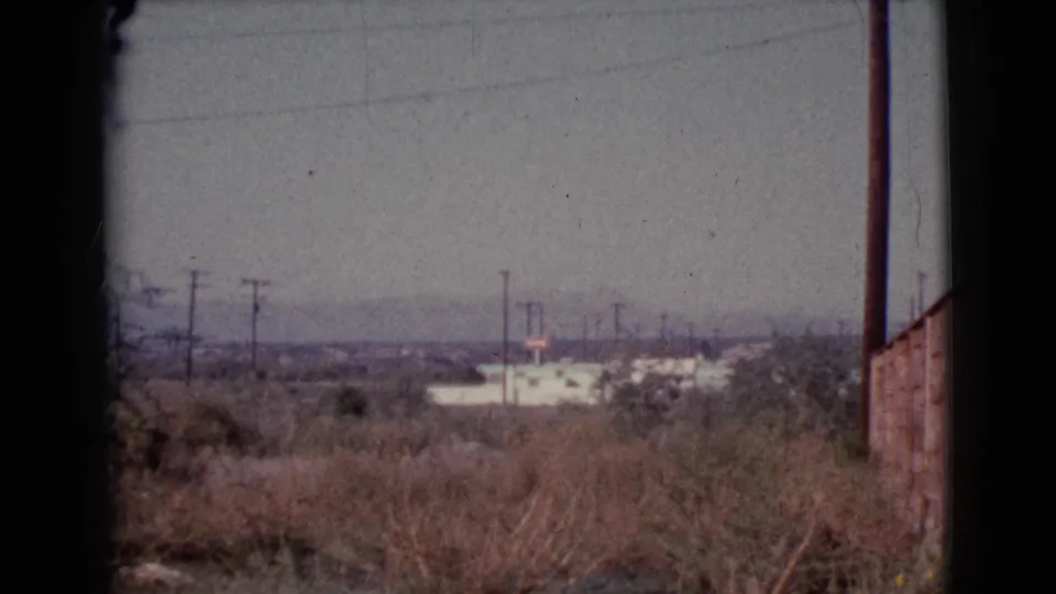 Cottonwood, Arizona frame with dry roadside vegetation, utility poles, distant low buildings, hazy hills, and a wall at the right edge.