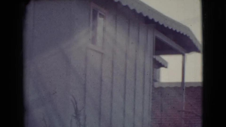 1964 Cottonwood, Arizona frame with the side of a wood-sided house, small window, corrugated roofline, and a shaded porch edge in the background.