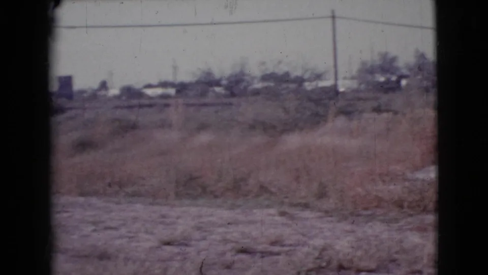 1964 Cottonwood, Arizona outskirts view with dry vegetation, overhead wires, utility poles, and distant town structures.