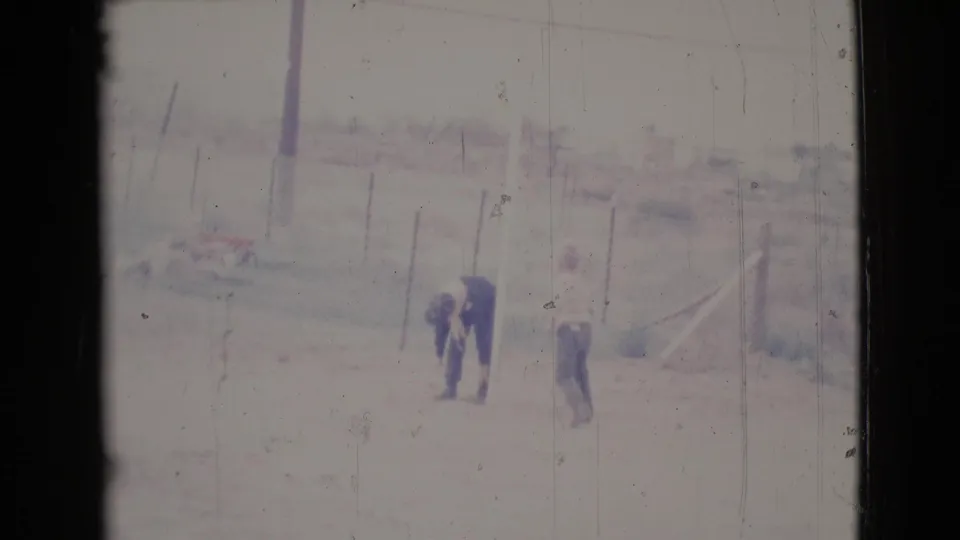 A distant adult bends toward the ground or clothing while another adult stands nearby in the Cottonwood yard scene.