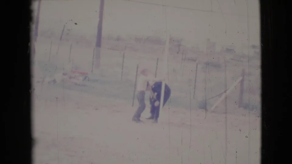 The 8mm frame shows one adult bending toward another person's pant leg in a bright fenced yard in Cottonwood, Arizona.