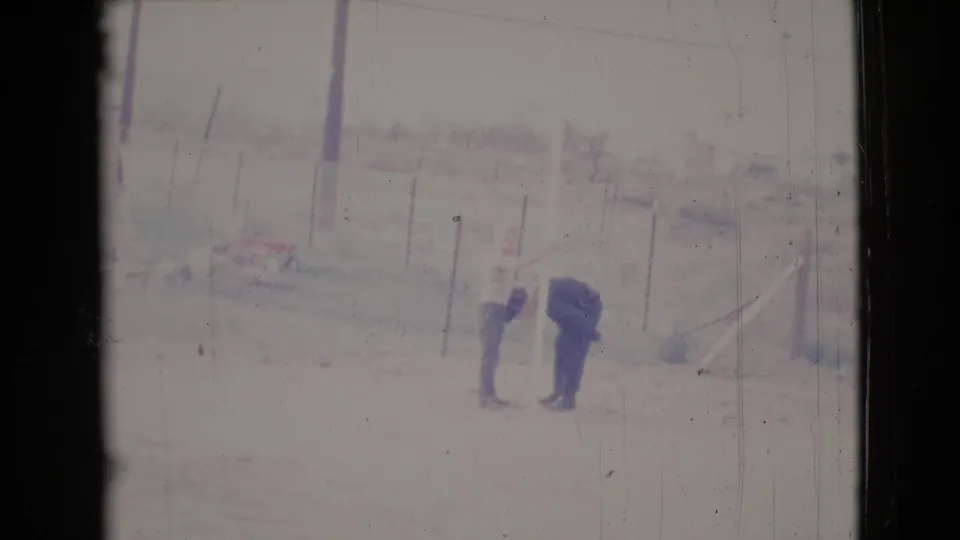 Two distant adults lean toward each other in the 1964 Cottonwood yard, suggesting attention to clothing or dust on pants.
