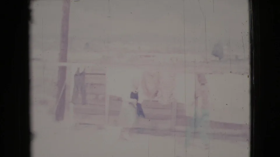 A faded Cottonwood 1964 frame shows a woman near the laundry line, with another partly obscured figure and porch details behind her.