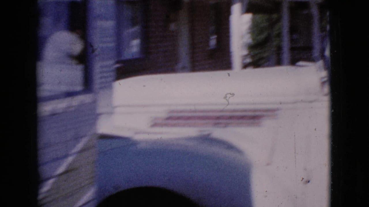 White pickup truck passing close to the camera beside a house or porch.