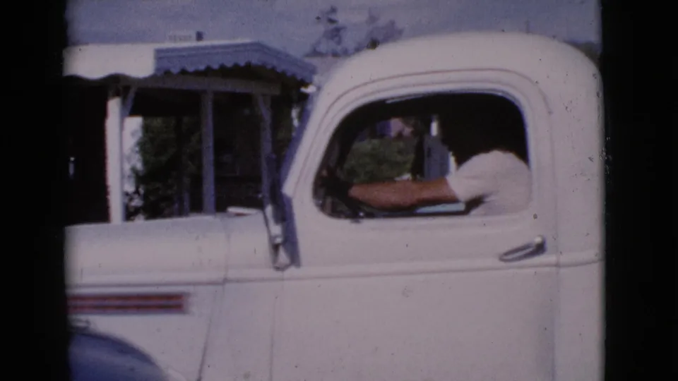 1964 Cottonwood, Arizona frame showing a man in a white pickup cab with porch details behind the vehicle.