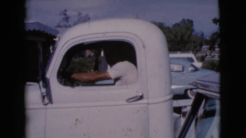 1964 Cottonwood, Arizona frame of the white pickup cab, with the driver visible and other cars parked in the background.
