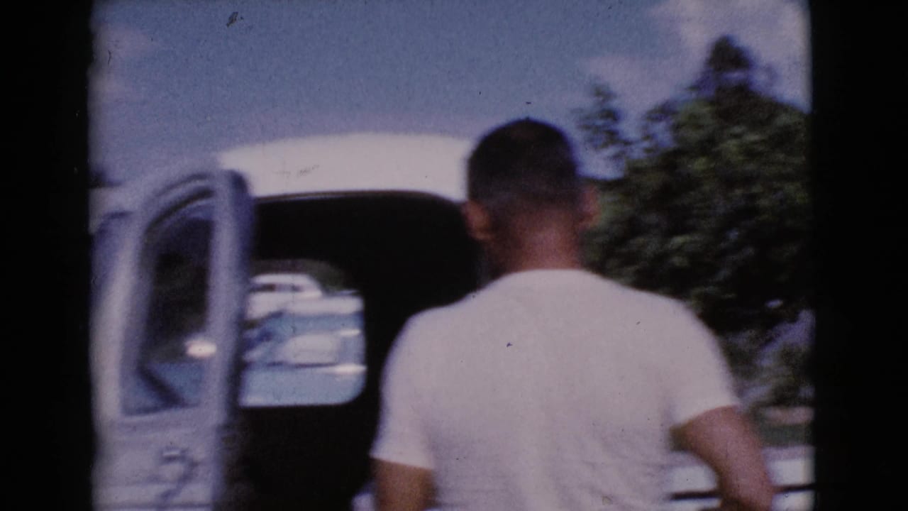 Man in a white T-shirt approaches an open white pickup truck door outdoors.
