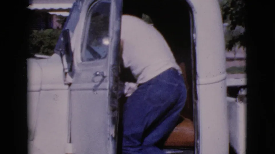 The man leans into the driver's side of the white pickup, with the truck cab and door filling most of the 1964 Cottonwood frame.