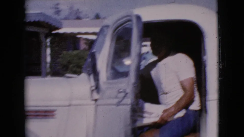 The man is partly seated inside the open driver's side of the white pickup, with the sunlit Cottonwood setting visible behind the cab.