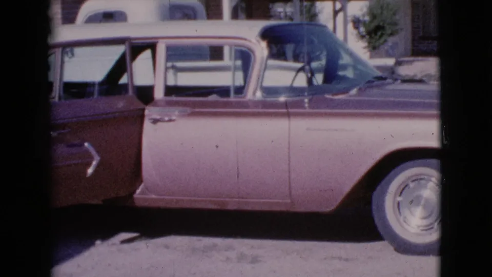 The sedan remains parked in the 1964 Cottonwood, Arizona street scene, now seen with an open door and residential houses behind it.