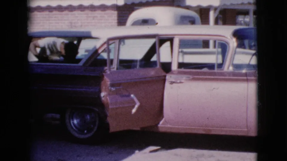 1964 Cottonwood, Arizona frame with a man in a light shirt leaning into the back of a two-tone station wagon near a white RV trailer.