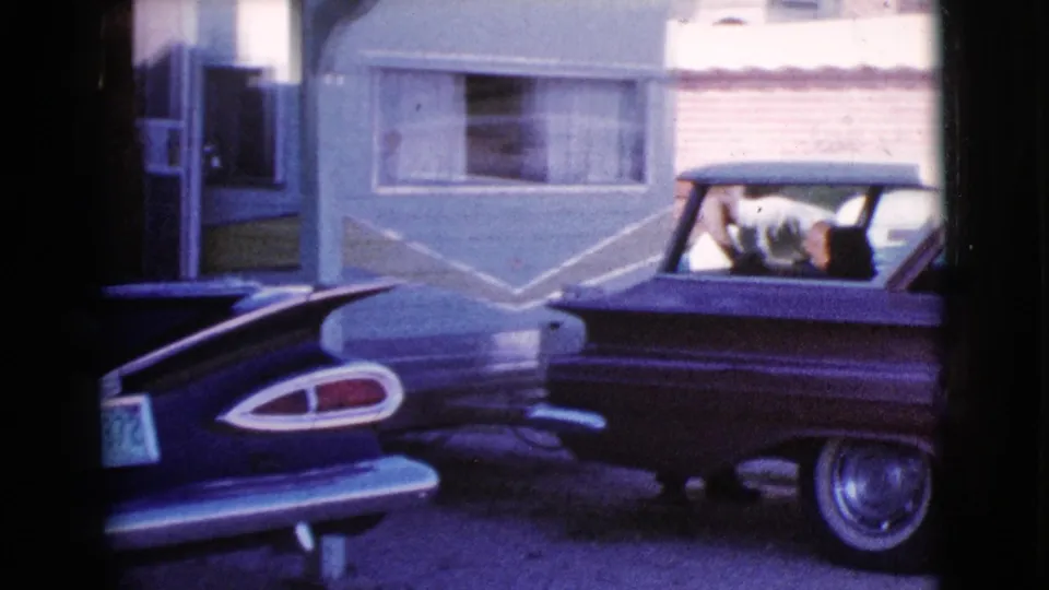 A 1964 Cottonwood car-lot view shows a dark vintage sedan near a light blue trailer and another parked car.