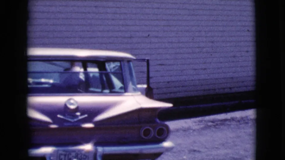 Rear view of a purple and white 1960s sedan in Cottonwood, Arizona, with a plain wall behind it.